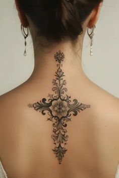 the back of a woman's neck with an intricate cross tattoo on her lower back