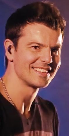 a close up of a person with a smile on his face and wearing a necklace