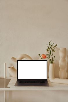 an open laptop computer sitting on top of a white table next to vases and candles