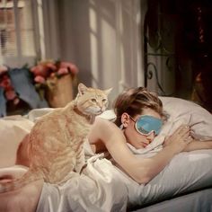 a woman laying in bed with a cat on her lap next to her sleeping mask