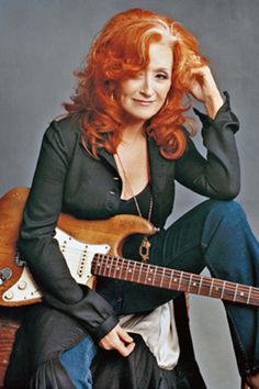 a woman with red hair is holding a guitar