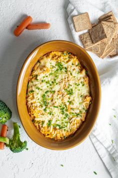 an overhead view of a casserole dish with broccoli, carrots and crackers