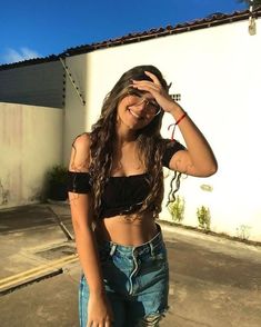 a woman standing in front of a white building with her hands on her head and wearing ripped jeans