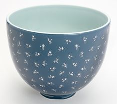 a blue bowl with small white flowers on the outside and inside, sitting on a white surface