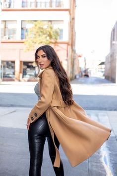 a woman in black leather pants and a camel coat