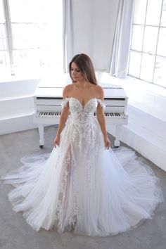 a woman standing in front of a white piano wearing a wedding dress with an off the shoulder train