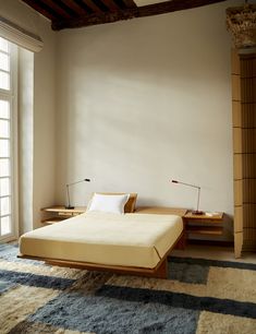 a bed sitting in the middle of a bedroom next to a dresser and lamp on top of a rug