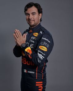 a man with his hands folded in front of him, wearing a racing suit and smiling at the camera