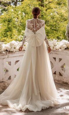 a woman in a wedding dress standing on a stone wall with white flowers behind her