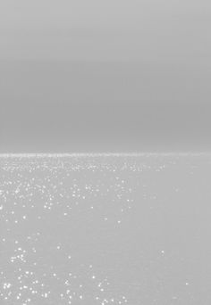 a lone boat in the middle of an ocean on a foggy day with light reflecting off the water