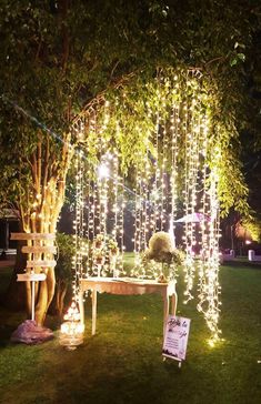 a bench under a tree covered in fairy lights and string lights for a wedding ceremony