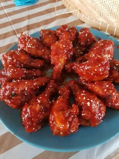 a blue plate topped with chicken wings covered in sauce on top of a striped table cloth