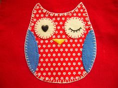 an embroidered owl on a red shirt with white and blue flowers around its eyes is shown