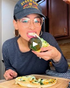 a woman in glasses is eating some food on a cutting board and looking at the camera