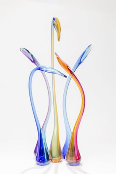 three colorful glass vases sitting on top of a white table next to each other