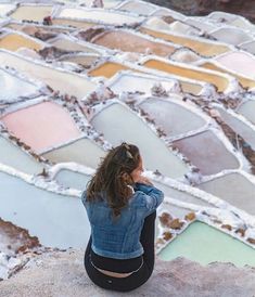 a woman sitting on top of a rock looking down