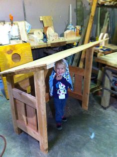 a young child standing in front of a table made out of wooden planks and plywood