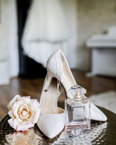 a pair of white high heels sitting on top of a table next to a bottle of perfume