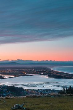 the sky is pink and blue as the sun sets over a lake with mountains in the background