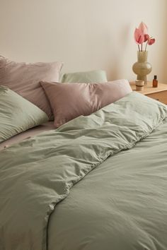 an unmade bed with green sheets and pink pillows in a white room next to a window