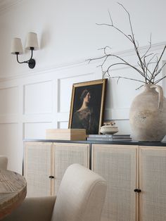 a white vase sitting on top of a wooden cabinet next to a table with chairs