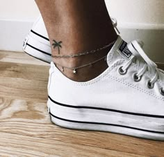 a person wearing white tennis shoes with a small palm tree tattoo on their ankle chain