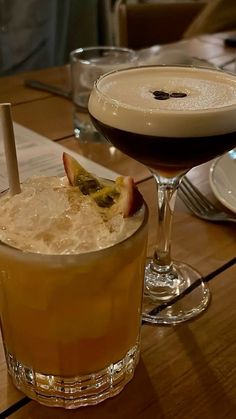 two glasses filled with drinks sitting on top of a wooden table next to plates and utensils