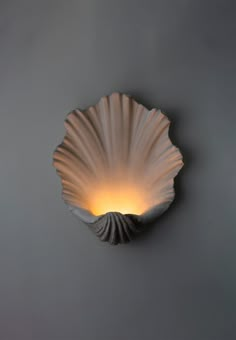 a scallop shell shaped light fixture mounted on a gray wall with dim lighting