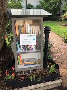 a book stand with books on it in the middle of a yard next to a tree