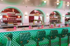 the interior of a bar with green chairs and checkered counter tops, along with shelves full of liquor bottles