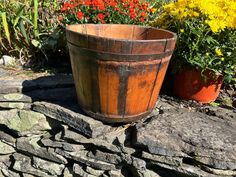 a wooden bucket sitting on top of a stone wall next to flowers and plants in the background