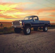 a blue pickup truck parked on the side of a road in front of a sunset