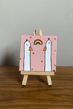 a small easel with two ducks on it and a rainbow painted on the side