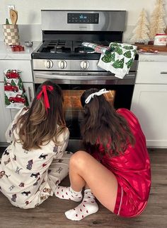 two women sitting on the floor in front of an oven with christmas decorations around them