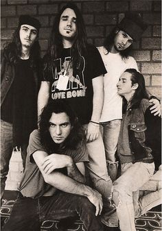 five young men standing next to each other in front of a brick wall