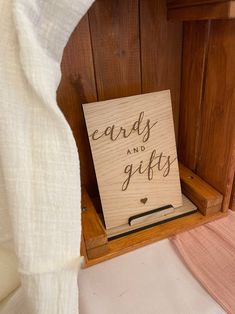 a wooden sign that says cards and gifts in black lettering on it, sitting next to a bed