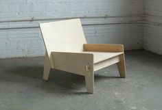 a wooden chair sitting on top of a cement floor next to a brick wall with white paint