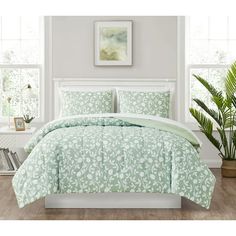 a bed with green comforter and pillows in a room next to a potted plant