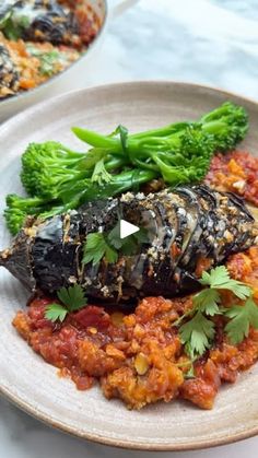 a white plate topped with an eggplant covered in sauce and broccoli