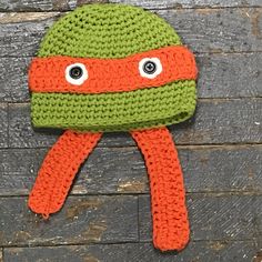 an orange and green knitted hat with googly eyes on top of a wooden surface