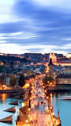 the city is lit up at night and people are walking on the bridge over the water