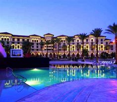 an outdoor swimming pool in front of a large building with multiple balconies at night