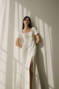 a woman standing in front of a white wall wearing a dress with slits on the side