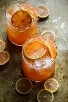 two glasses filled with orange juice and garnished with limes