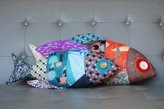 a colorful fish pillow sitting on top of a gray couch next to a white wall