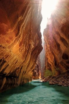 the sun shines brightly in between two narrow canyons, with blue water running through them