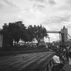 black and white photograph of people sitting on benches in front of tower bridge