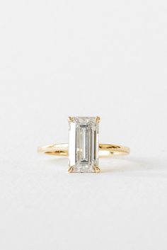 a yellow gold ring with an emerald cut diamond in the center, on a white background