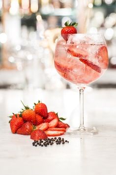 a glass filled with ice and strawberries on top of a counter next to some wine glasses