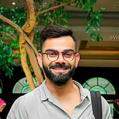 a man with glasses and a beard standing in front of a tree smiling at the camera